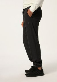 Svarta joggingsbyxor med elastiska muddkanter, dragsko i midjan, sidofickor och en subtil texturerad mönster. Bärs med svarta sneakers.