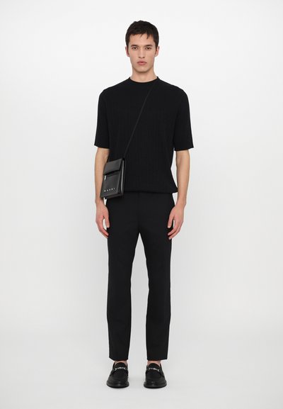 Top negro de manga corta acanalado, pantalones negros ajustados y mocasines negros. Un pequeño bolso cruzado negro está colgado del cuerpo.