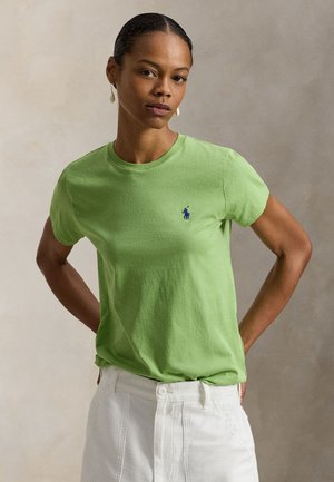 Tricou verde din bumbac, cu guler rotund și mânecă scurtă, având un logo brodat albastru pe partea stângă a pieptului. Împreună cu pantaloni albi.