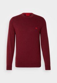 Pull pour homme à manches longues et col rond de couleur rouge foncé, avec des poignets et un ourlet côtelés, comportant une petite écusson rouge sur la poitrine.