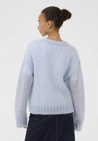 Pull en mohair bleu clair avec une coupe décontractée, ourlet côtelé, épaules tombantes et texture douce. Dispose d'un col en V et de coutures minimalistes.