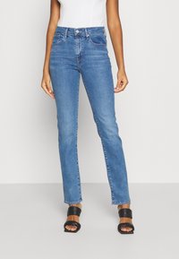 Hoch geschnittene hellblaue Jeans aus Stretch-Denim mit klassischem geradem Bein, subtiler Ausbleichung und vorderen Taschen. Schwarze Absatzsandalen.
