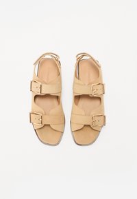 Sandale din suede de culoare tan, cu două curele late și catarame de culoare aurie. Design cu vârf deschis și tălpic căptușit, talpă plată.