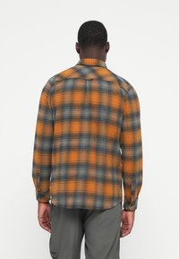 Camisa de franela a cuadros con patrones en naranja, gris y azul; presenta un diseño de yugo, mangas largas, puños abotonados y un dobladillo recto.
