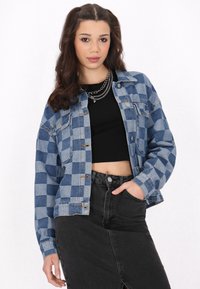 Blå och grå rutiga jeansjacka med knappstängning och fickor, kombinerad med en svart kort topp och en högmidjad svart jeanskjol.