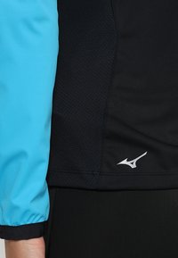 Blue and black athletic top with textured fabric, logo accent in silver, and elastic cuff detailing on the blue sleeve.