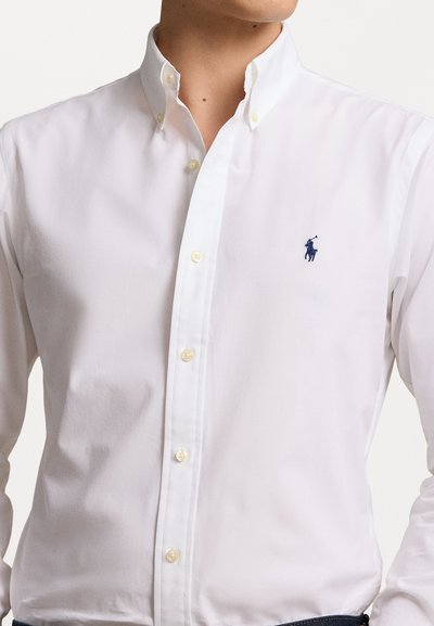 Witte katoenen overhemd met knopen, voorzien van een klassieke kraag, parelknopen en een klein marineblauw logo op de borst. Gladde textuur en getailleerde pasvorm.