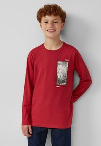 Rode langwerpige t-shirt gemaakt van katoen, met een graphic print in zwart-wit en tekstaccenten. Ronde hals en een losse pasvorm.