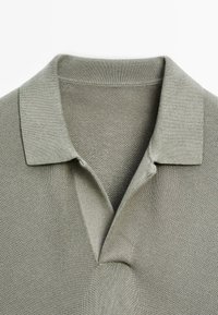 Col de polo tricoté vert olive clair avec un motif texturé subtil et une patte de boutonnage ouverte.