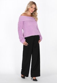 Lilafarbenes Off-Shoulder-Pullover mit flauschiger Textur, kombiniert mit schwarzen weiten Hosen und Punkten-Heels. Silberne Halskette als Akzent.