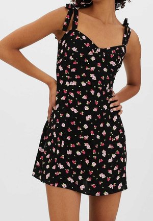 Robe noire à motif floral rose et blanc. Dotée de bretelles fines avec des accents de nœuds, d'un corsage ajusté et d'une jupe évasée. Texture de tissu doux.