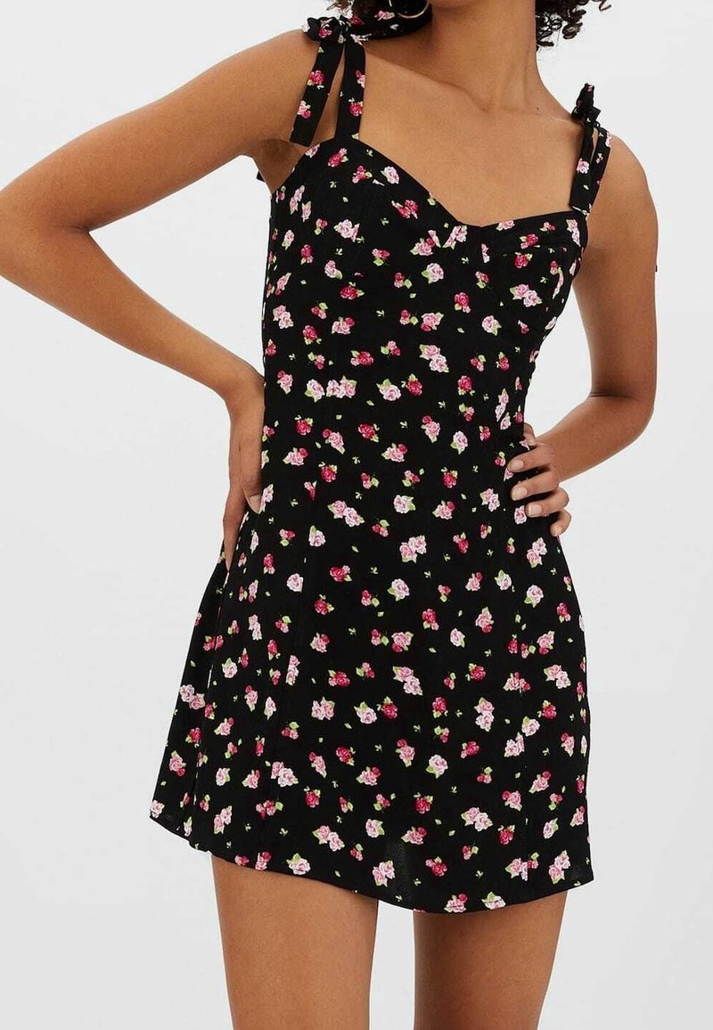 Robe noire à motif floral rose et blanc. Dotée de bretelles fines avec des accents de nœuds, d'un corsage ajusté et d'une jupe évasée. Texture de tissu doux.