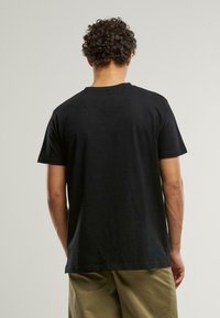 Tricou negru din bumbac, cu mâneci scurte și guler rotund, având spatele simplu, fără logo-uri sau modele vizibile.