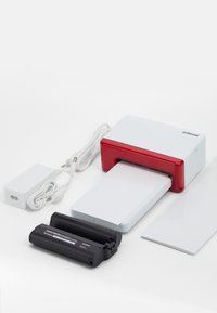 Polaroid photo printer in white with a red accent, includes a power adapter, rechargeable battery, and several photo-sized papers.