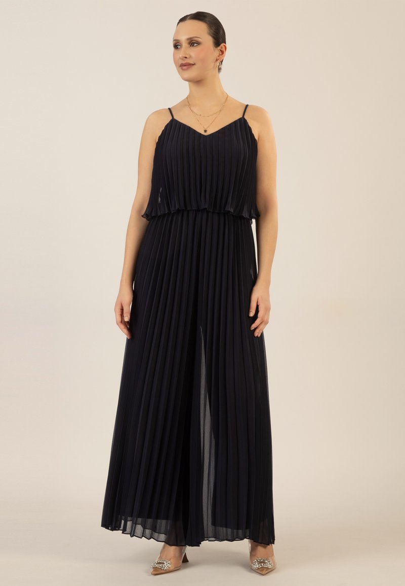 Jumpsuit plisado marino con un cuerpo en capas, tirantes finos y un diseño fluido. Presenta un delantero partido y una tela suave y ligera.