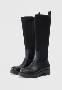 Bottes noires montantes dotées d'une semelle en caoutchouc lisse, d'un tige en tissu texturé, de fermetures éclair sur les côtés et de tirettes pour un enfilage facile.