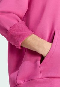 Lyserød sweatshirt med en tekstureret strikfinish, synlig lomme og ribbede manchetter. Ærmet er let opsmøgget.
