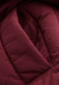 Tissu matelassé bordeaux plié avec des lignes de couture visibles, suggérant un vêtement ou une couverture épaisse et rembourrée.