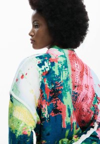 Suéter de punto colorido con un patrón abstracto en verde, rosa, azul y rojo. La textura parece suave, con un ajuste relajado y hombros caídos.