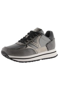 Zapatilla deportiva gris que presenta una mezcla de cuero y materiales sintéticos, cordones negros, una entresuela blanca y detalles texturizados en la parte superior.