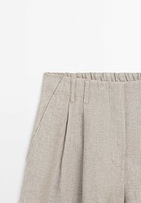 Pantaloni grigi chiari realizzati in tessuto texturizzato, con un design plissettato, vita elastica e tasche laterali. Dettaglio a righe visibile.