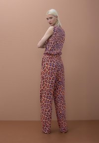 Mono sin mangas con estampado de leopardo en naranja y morado, de ajuste holgado con cinturilla alta y piernas anchas, confeccionado en tela ligera.