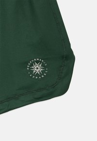 Πράσινο αθλητικό σορτς από μαλακό ύφασμα, με κυκλικό λογότυπο που γράφει "Performance Apparel" σε λευκό. Στρογγυλό τελείωμα και ραμμένα άκρα.