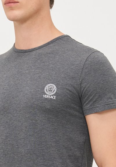 Graues Baumwoll-T-Shirt mit kurzen Ärmeln, das auf der linken Brust ein weißes Versace-Logo und ein Löwenemblem zeigt. Rundhalsausschnitt, enganliegendes Design.