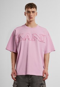 Ružičasta oversized majica kratkih rukava s istaknutim izvezenim logom "KANY" na prednjoj strani. Napravljena od mekog pamuka, glatke teksture.