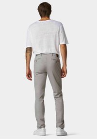 Pantalons gris clair ajustés, avec une texture lisse et un motif subtil. Assortis à une chemise blanche à manches courtes et des baskets blanches.