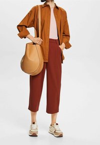 Camisa de botones marrón, top rosa, pantalones cortos burdeos, zapatillas beige y marrón, y un bolso de hombro color tostado con un diseño curvado.