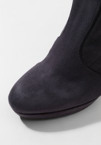 Stivale alla caviglia in suede viola scuro con punta rotonda e superficie liscia, caratterizzato da cuciture minime e un design semplice.