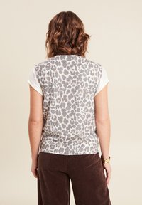 Korte mouw top van een lichte stof met een grijs en beige luipaardprint op een witte achtergrond, gecombineerd met bruine corduroy broek.
