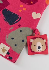 Helles pinkes Gewebe mit abstrakten Formen in verschiedenen Farben, versehen mit einem grauen Patch und einem roten Stoffetikett, das eine Bärenkopf-Illustration zeigt.