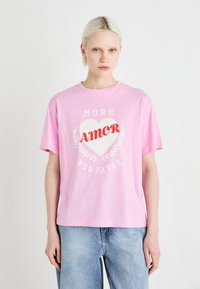Růžové bavlněné tričko s krátkým rukávem, které má bílé srdce a červený nápis "AMOR" s "MORE" a "POR FAVOR" v světle šedé.