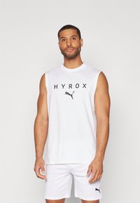 Biely tielko bez rukávov s čiernym nápisom "HYROX" a logom Puma. Nosí sa s bielymi šortkami s malým čiernym logom Puma. Čistý, minimalistický dizajn.