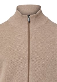 Beiger gestrickter Reißverschluss-Pullover mit hohem Kragen, aus strukturiertem Stoff und einem silbernen Reißverschluss in der Mitte.