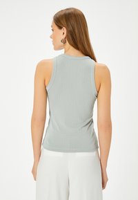 Lys grå ribbet tanktop med en tætsiddende design, rund halsudskæring og ærmeløs skæring. Glat stoftekstur. Vist fra bagsiden.