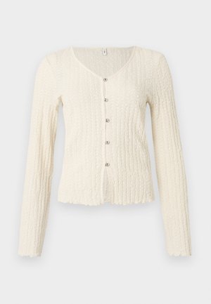 Ελεφαντόδοντο πουλόβερ με μακριά μανίκια και υφασμένο μοτίβο, με V-λαιμόκοψη και πέντε μεταλλικά κουμπιά μπροστά. Στρογγυλεμένο τελείωμα.