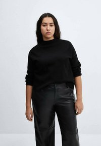Maglione nero a maglia con scollatura alta, abbinato a pantaloni larghi in pelle nera. La texture del maglione è liscia e la vestibilità è comoda.