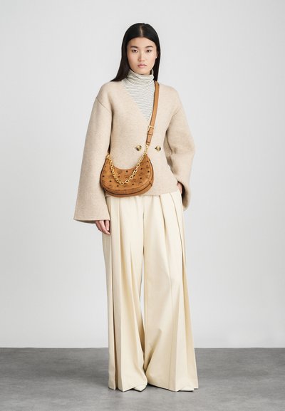 Veste oversize en mélange de laine beige avec des manches évasées, associée à un col roulé rayé et un pantalon large crème. Sac à main marron avec chaîne dorée.