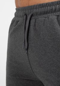Donkergrijze sweatpants met een elastische tailleband, voorzien van een trekkoord en een gladde textuur. Geen zichtbare zakken of patronen.