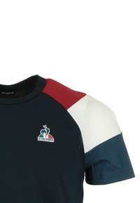 T-shirt blu navy con design color block e accenti rossi, bianchi e blu. Include un logo sul lato sinistro del petto. Materiale morbido in cotone.