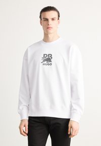 Hvit bomullssweatshirt med et grafisk logo i grå, rund halslinning, ribbestrikkede mansjetter og kant, samt svart bukse.