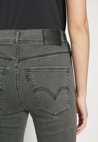 Personne portant un jean Levi's noir délavé avec des poches arrière visibles et une étiquette en cuir de la marque sur la ceinture, associée à un haut noir.