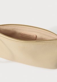 Kremasta torbica od kože s teksturom i zlatnim patentnim zatvaračem. Unutrašnjost je obložena bež tkaninom s oznakom na kojoj piše "Coccinelle Autentična talijanska koža".