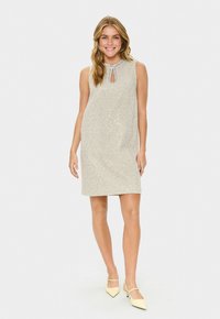 Beiges ärmelloses Kleid mit Pailletten, runder Halslinie und Schlüssellochdetail. Getragen mit gelben, spitzen, niedrigabsatz Schuhen.