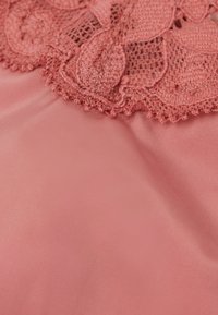 Koraalroze stof met ingewikkelde kantafwerking en een bloemmotief langs de bovenrand. Gladde textuur met fijne ribbeling zichtbaar.