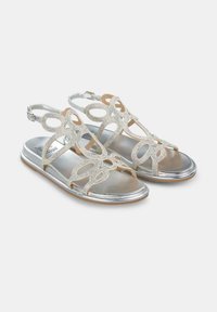 Silberne und cremefarbene Sandalen mit einem kunstvollen Design, das ausgeschnittene Muster und R rhinestone-Akzente auf einer metallischen Sohle präsentiert.