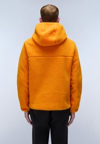 Orange fleecejacka med huva, med en texturerad yta och en avslappnad passform. Bakifrån syns sömdetaljer och en rak skärning.